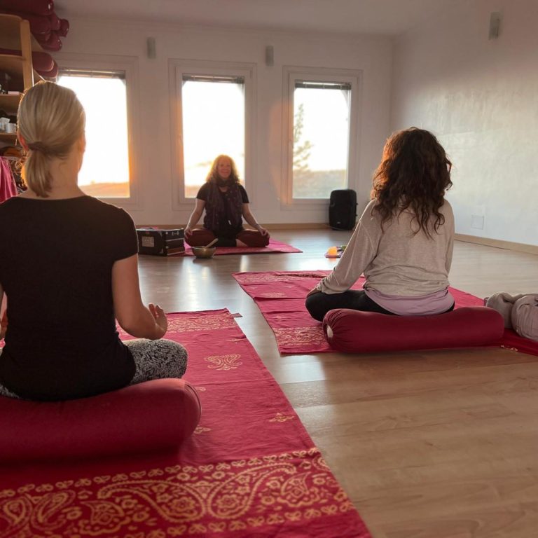 Eine Person in gelber Kleidung macht eine Yoga-Übung, Schatten auf der Wand sichtbar.